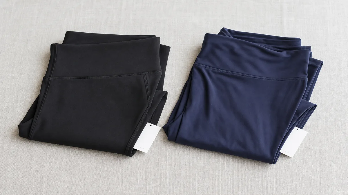 Image: two folded pairs of leggings side by side on a light surface, one matte and structured, one soft and draped, a price tag partially visible on each