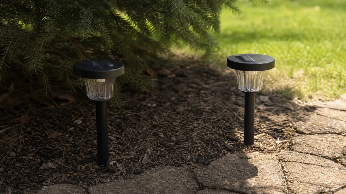 Image: a solar light installed in deep shade under overhanging tree branches next to a second identical light in full open sun, subtle visual contrast in how much daylight each panel receives — AI illustration